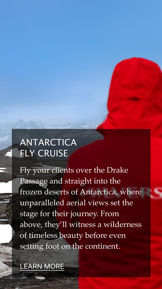 A person in a red jacket gazes at a snowy, mountainous landscape with an airplane flying above.