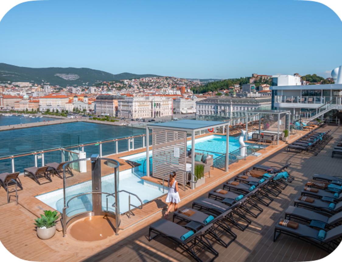 Cruise ship deck with pool, hot tub, and city view.