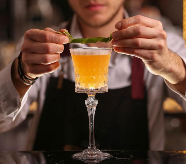 Bartender garnishing an orange cocktail with a green peel.