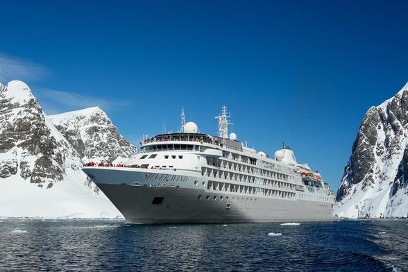 The Silver Wind cruise ship sailing through Antarctica's Lemaire Channel, flanked by snow-covered mountains.
